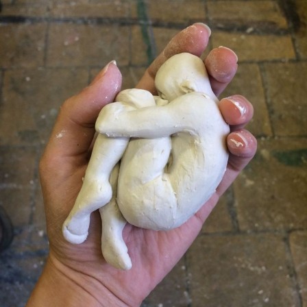un petit homme de glaise en position foetale dans la main d'une sculptrice