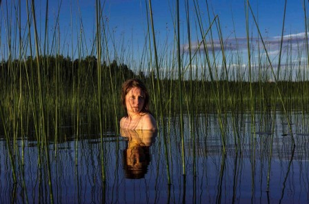 les épaules et la tête d'une femme émergent d'un plan d'eau avec roseaux et leur reflet donnent l'impression d'une figure de dame de jeu de carte, femme tronc au petit corps doublé
