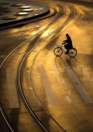 dans une lumière dorée sur la ville, un cycliste près d'une place où sa route croise la voie sinueuse du tramway