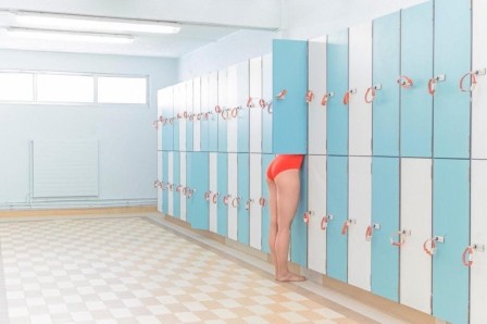 une femme en maillot de bain, le haut du corps caché par la porte de son casier de vestiaire où elle semble prête à disparaître