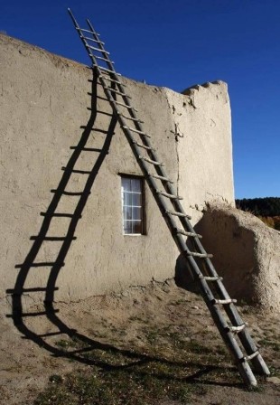 appuyée sur une maison, une échelle droite ; son ombre courbe sur le sol et le mur