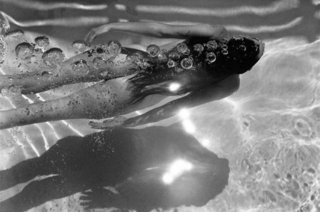 une femme nue nageant sous l'eau dans un nuage de bulles