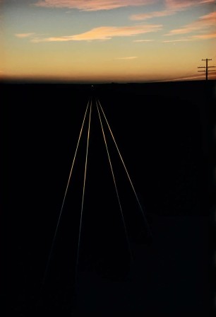 quatre rails sur le sol encore sombre traçant une ligne de fuite lumineuse vers l'infini sous le soleil levant