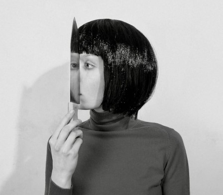 une femme de profil tient un couteau devant son visage, son oeil s'y reflète et nous regarde en face
