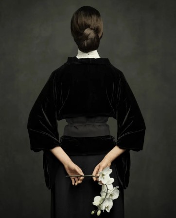 une femme en noir, de dos, tient derrière elle des fleurs blanches