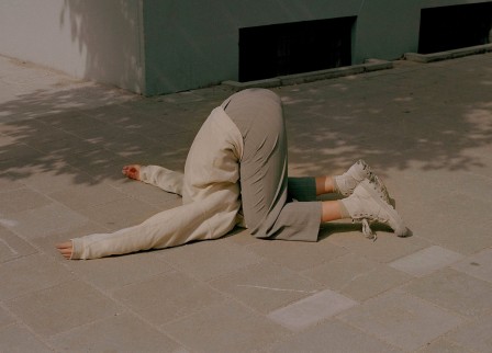 sur le trottoir, une femme à genoux, la tête entre les jambes et les bras tendus, dans la posture d'une roulade avant interrompue