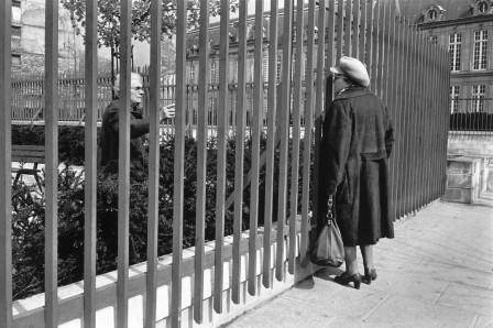 une femme observe un homme derrière les barreaux d'un jardin public