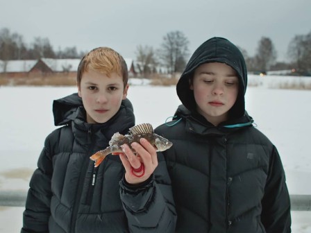 debout dans la neige en doudoune noire, deux jeunes garçons tiennent un petit poisson gelé