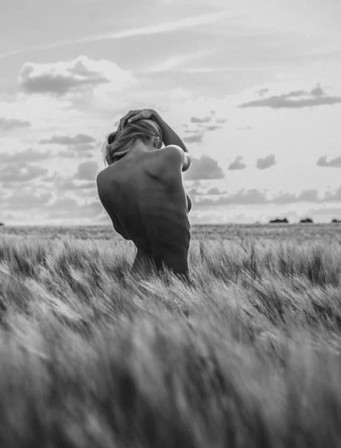 une agricultrice de dos, nue dans un champ de blé au lever du jour