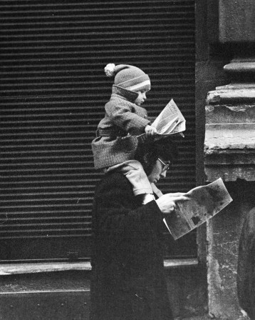un enfant lit le journal sur les épaules de son père qui lit le journal
