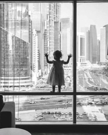 face à la ville, une petite fille debout sur le montant d'une fenêtre