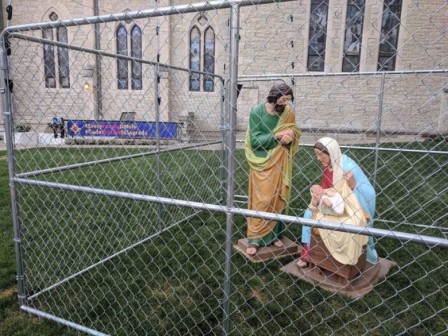 devant une église, une crèche de Noël entourée de hautes barrières grillagées