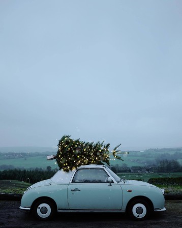 un sapin de Noël aux guirlandes allumées sur le toit, une voiture s'éloigne