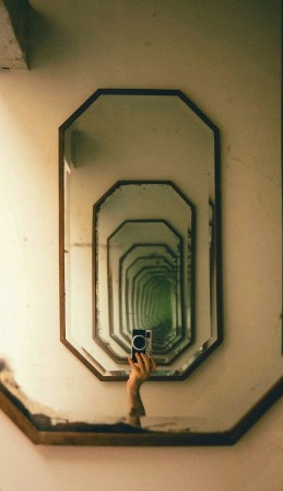 une main tenant un appareil photographique mise en abyme dans un tunnel de miroirs